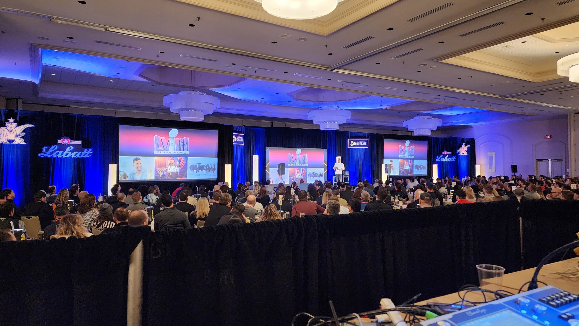 Wide conference room view of the AB InBev Supply Chain Conference stage, screens, and audience